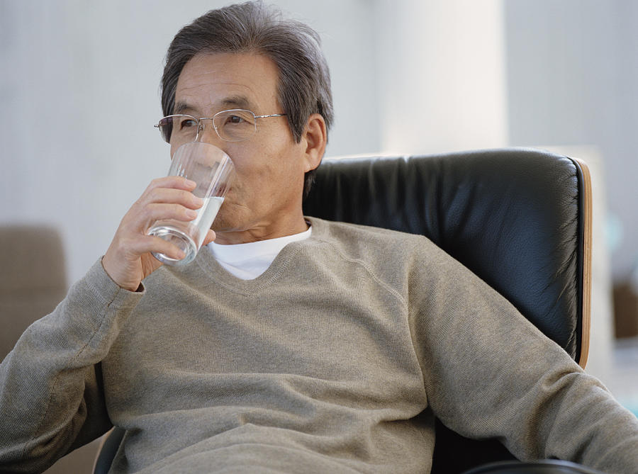 Senior man sitting on armchair drinking glass of water Photograph by Digital Vision