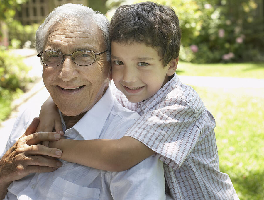 Senior man sitting outdoors with young boy being affectionate toward him and smiling Photograph by Sam Edwards