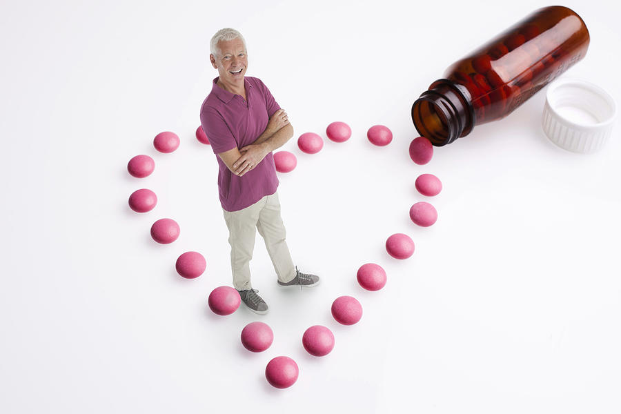 Senior man stands amongst heart-shaped pills Photograph by Andrew Bret Wallis