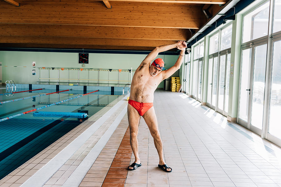 Senior man stretching by swimming pool Photograph by Eugenio Marongiu