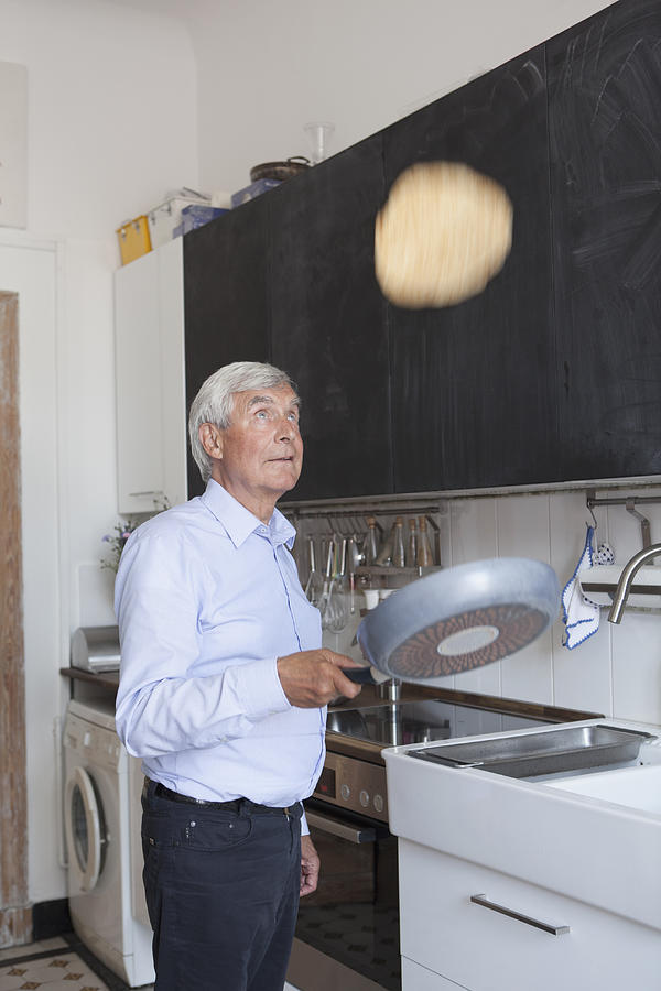 Senior man tossing pancake on frying pan in kitchen at home Photograph by Carl Smith