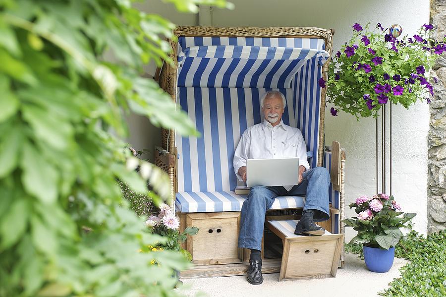 Senior man using laptop on garden seat Photograph by Karen Fox