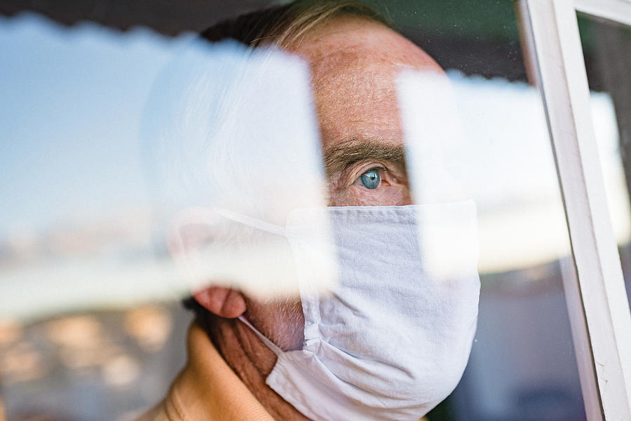 Senior man wearing face mask looking through the window Photograph by Igor Alecsander