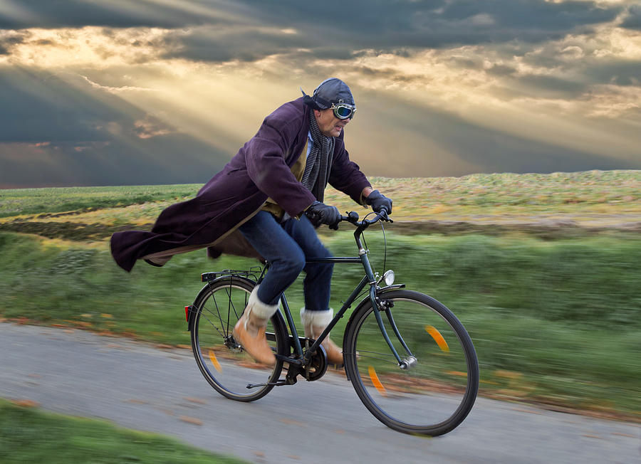 Senior man wearing leather helmet and retro aviator glasses cycling with blowing coat under dramatic skyscape Photograph by RelaxFoto.de