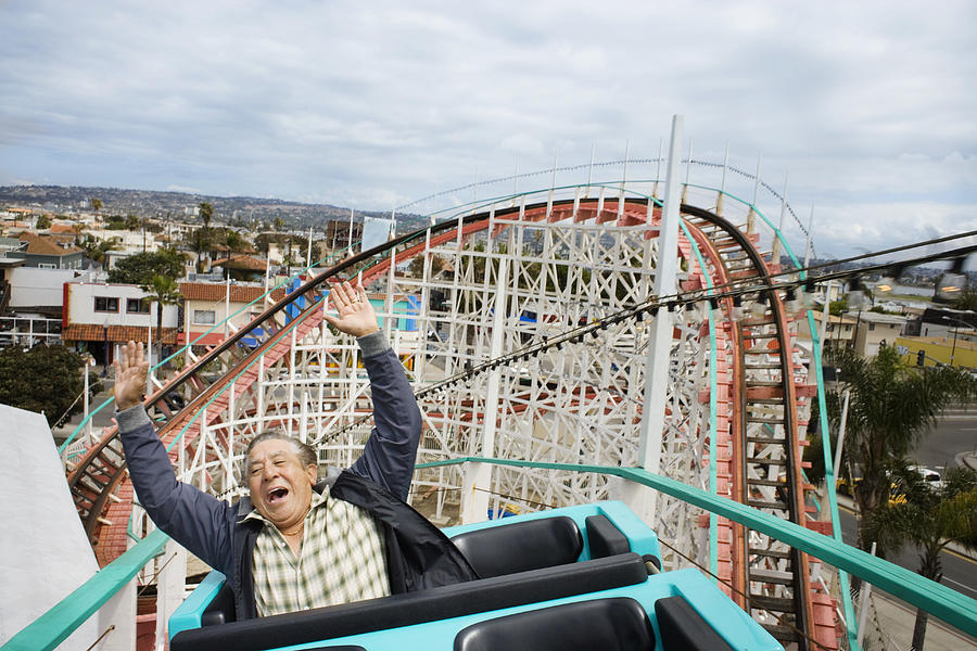 Senior man with hands raised, riding rollercoaster Photograph by Joe McBride