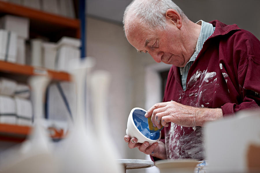 Senior potter painting a clay pot at workshop Photograph by Dean Mitchell