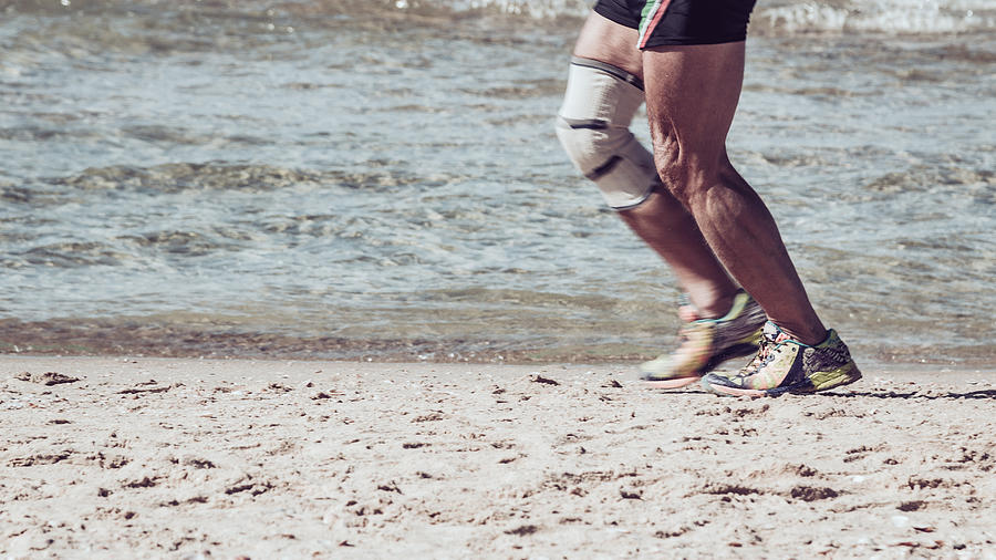 Senior with knee brace running on the beach Photograph by Kolderal