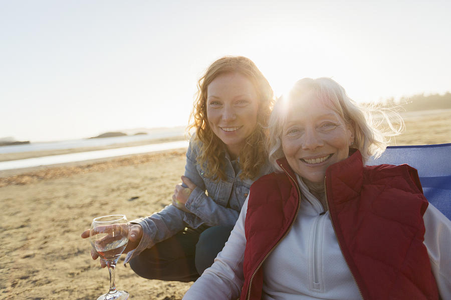 Senior woman and adult daughter relaxing on beach at sunset Photograph by Compassionate Eye Foundation/Steven Errico