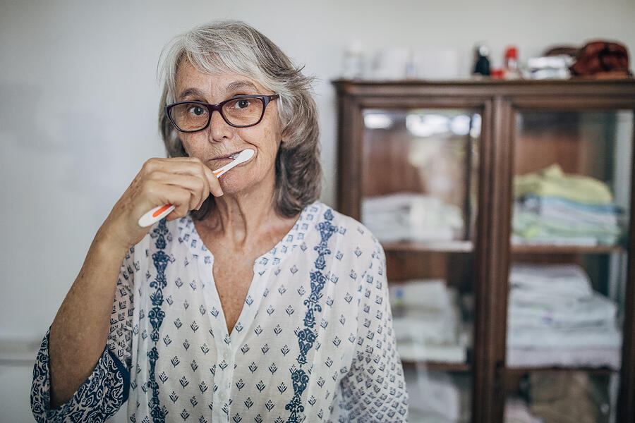 Senior Woman Brushing Teeth in Bathroom Photograph by South_agency