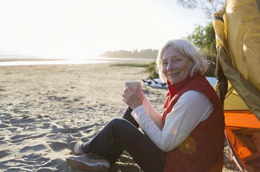 Senior woman camping on beach with coffee Photograph by Compassionate Eye Foundation/Steven Errico