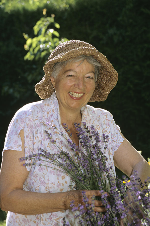 Senior woman holding lavender, smiling, portrait Photograph by Petrol