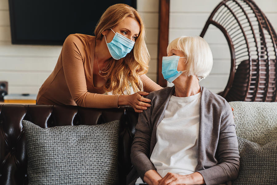 Senior woman in medical mask with social worker visiting her at home Photograph by Inside Creative House
