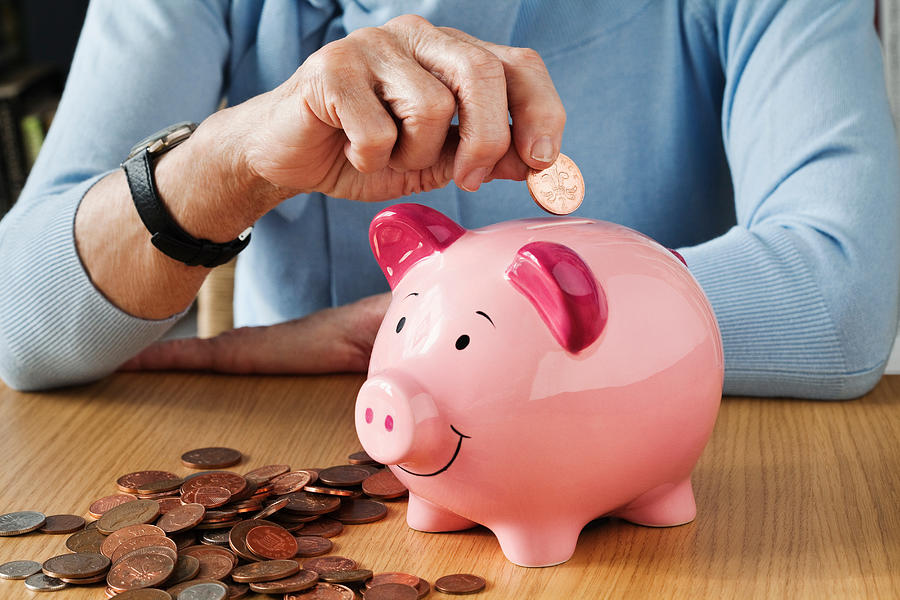 Senior woman inserting coins into piggybank Photograph by Image Source