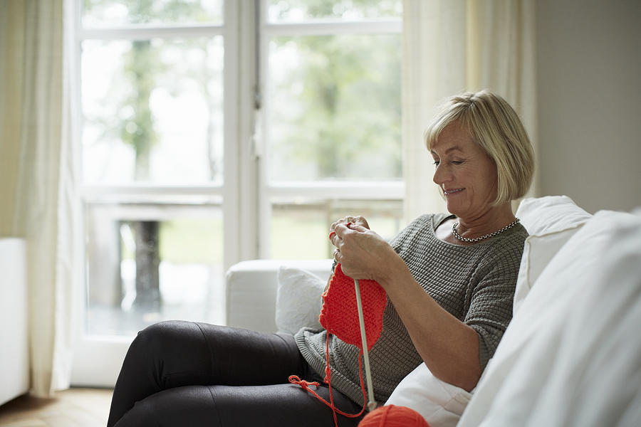 Senior woman knitting on sofa Photograph by Morsa Images