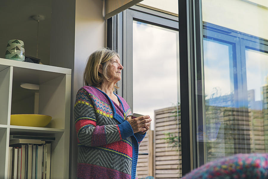 Senior woman looking out of window with a cuppa Photograph by Justin Paget