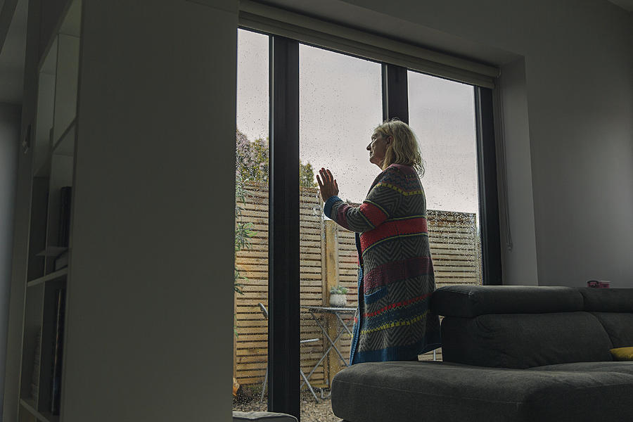 Senior woman looking through wet window Photograph by Justin Paget