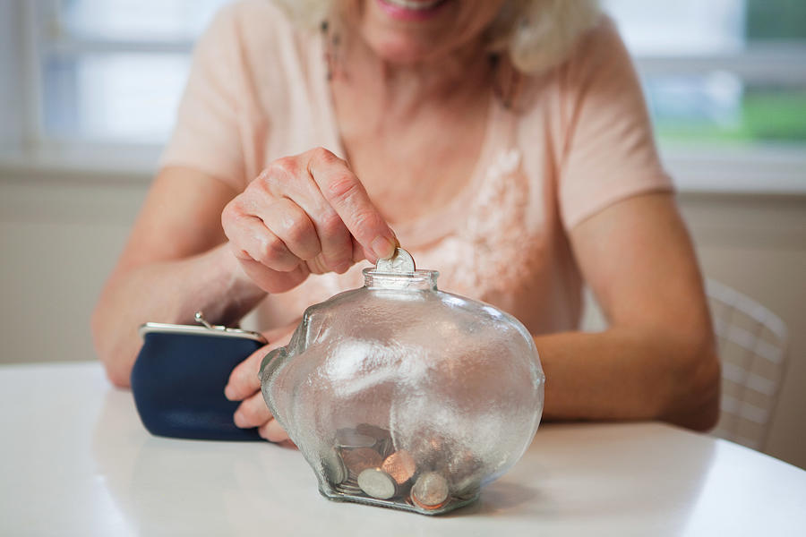 Senior woman saving money in piggy bank Photograph by Image Source