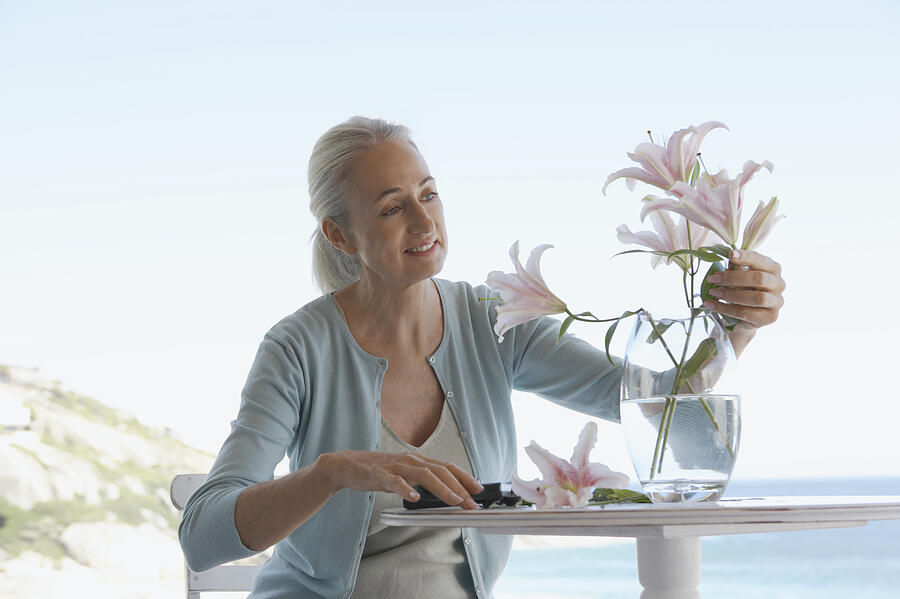 Senior Woman Sitting at a Table and Pruning Cut Flowers Photograph by Digital Vision.