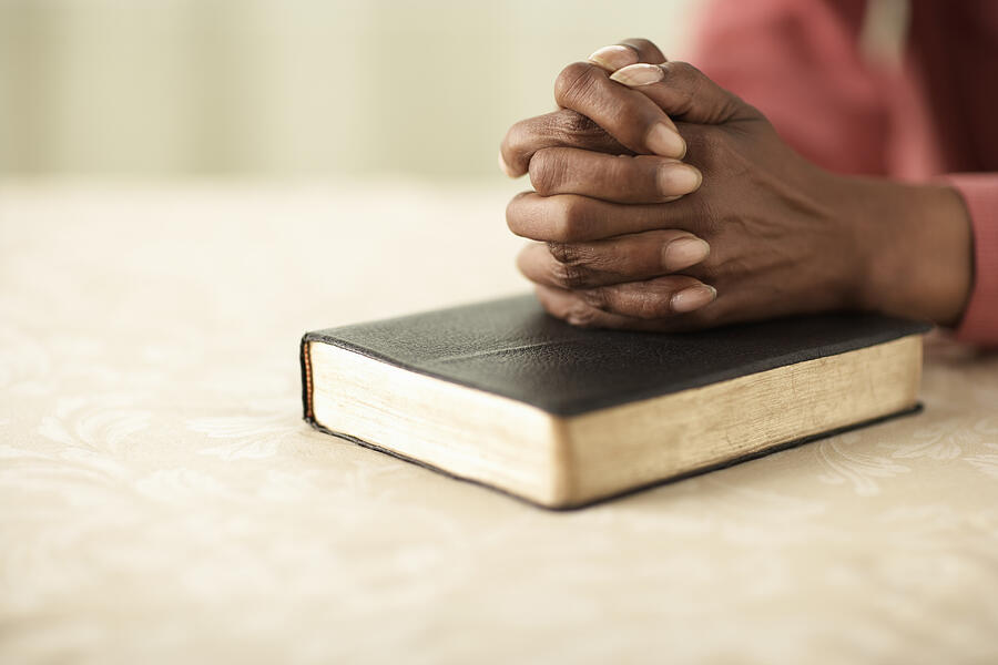 Senior woman sitting at table with hands clasped on Bible, close-up of hands Photograph by Thomas Northcut
