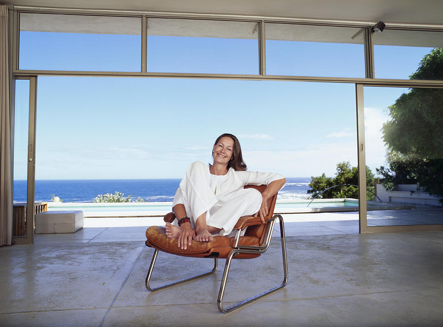 Senior Woman Sitting in a Modern Room with the Sea in the Background Photograph by Digital Vision.