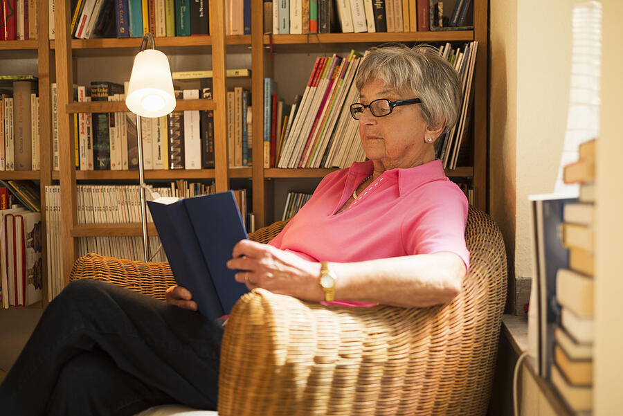 Senior woman sitting in armchair reading book Photograph by Cultura RM Exclusive/Attia-Fotografie