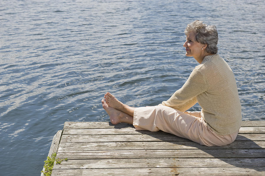 Senior woman sitting on dock Photograph by Tetra Images