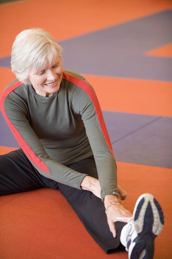 Senior woman sitting on floor, stretching Photograph by Caroline Woodham