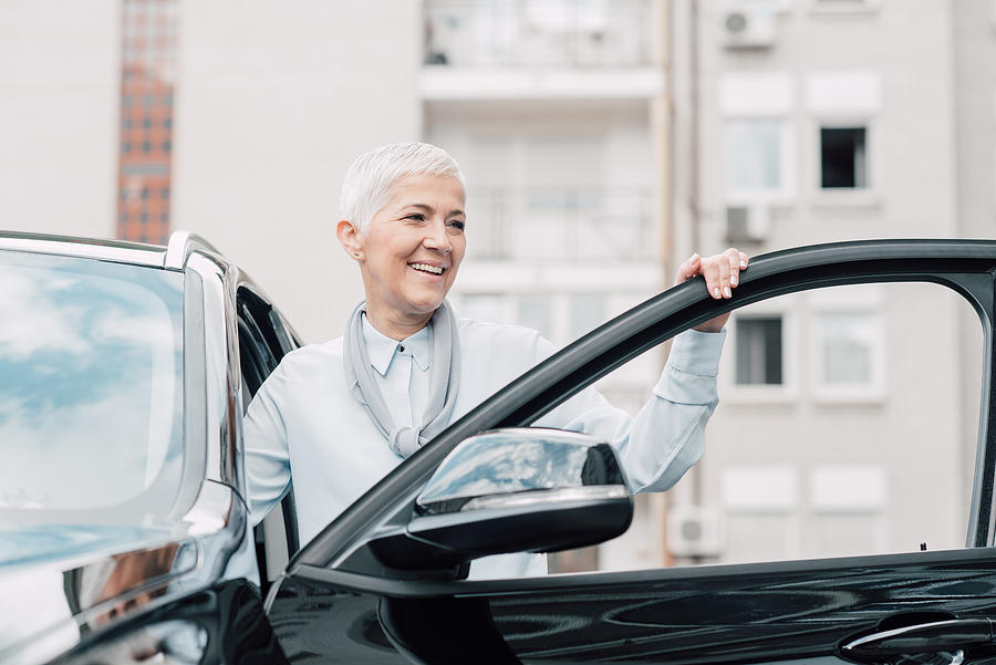 Senior woman smiling while entering a car Photograph by RgStudio