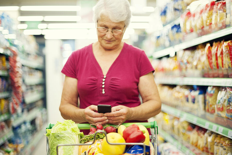 Senior woman texting on mobile phone at supermarket Photograph by Gpointstudio