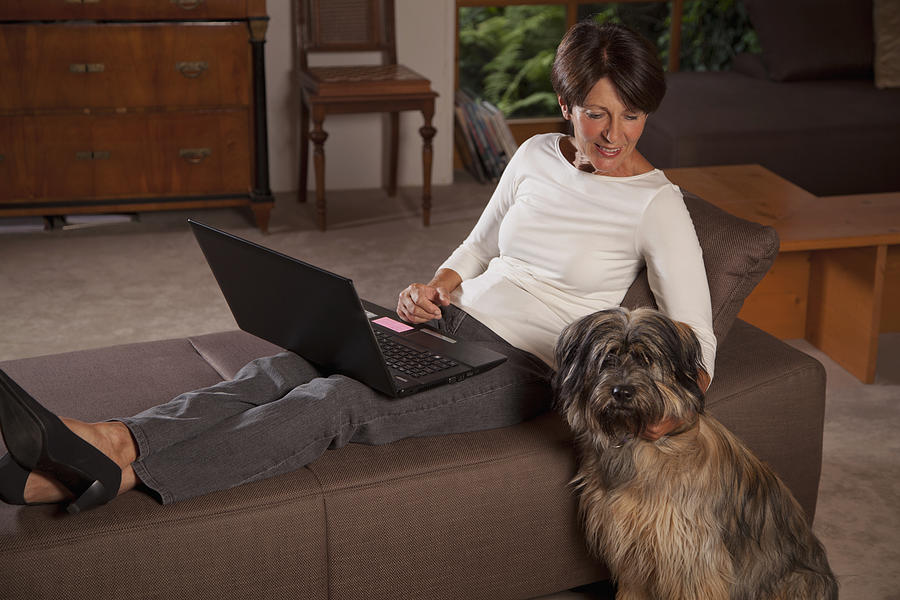 Senior woman using laptop, dog sitting beside Photograph by Birgid Allig