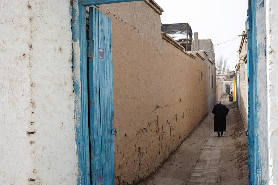 Senior woman walking along alley admist mud-brick houses in Kuqa,China Photograph by Xia Yuan