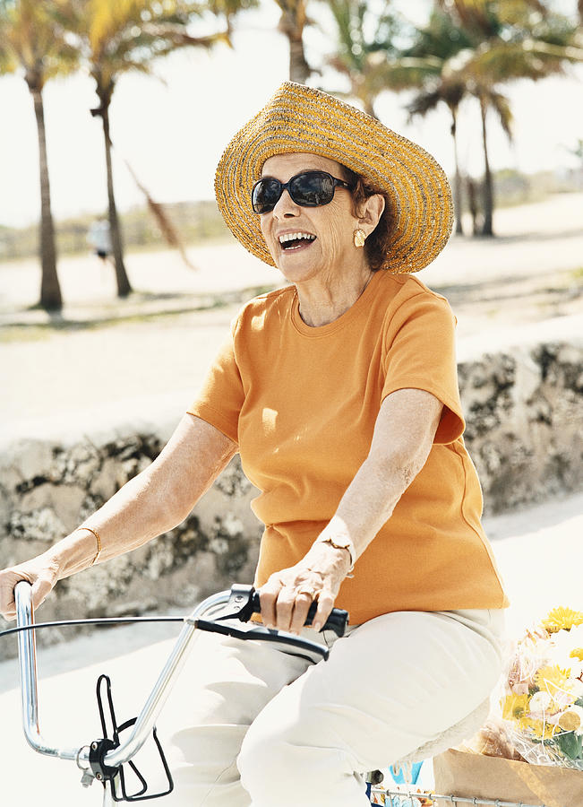 Senior Woman Wearing a Sun Hat and Riding a Bicycle Photograph by Digital Vision.