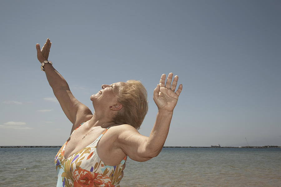 Senior woman wearing swimming costume on beach, arms raised, smiling Photograph by Dylan Ellis