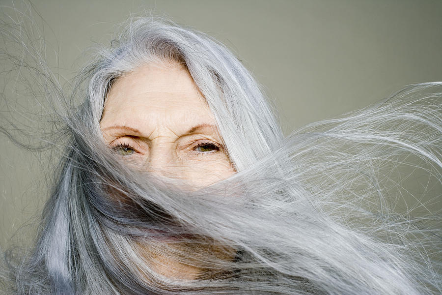 Senior woman with long hair blowing across face, portrait, close-up Photograph by Dan Kenyon