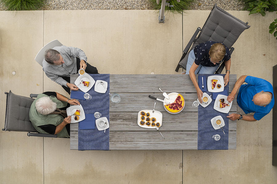 Seniors Enjoying Afternoon Coffee In Garden On Long Table View From Above Photograph by Amriphoto