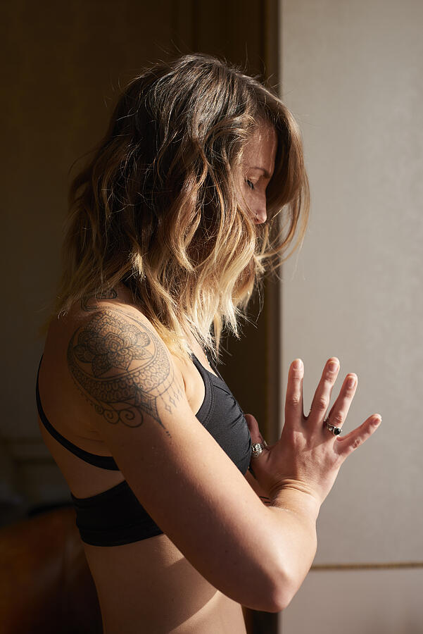 Serene woman with tattoo meditating with hands at heart center, anjali mudra Photograph by Caia Image