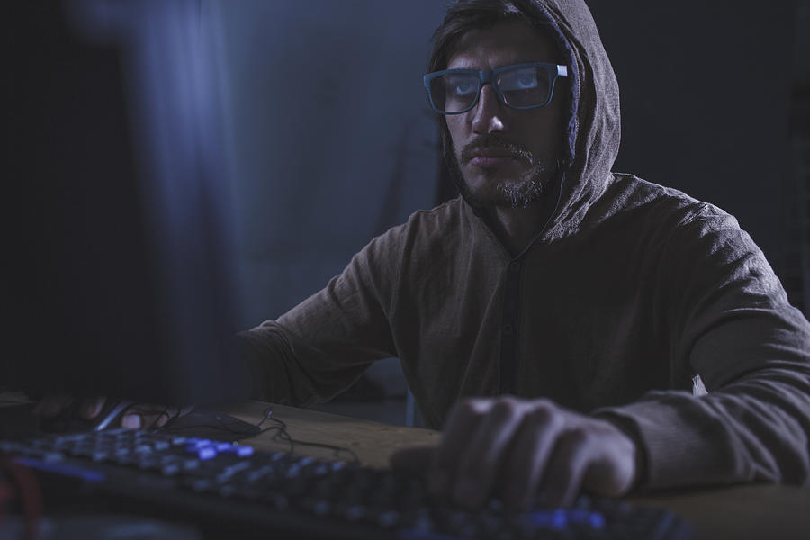 Serious burglar wearing hooded shirt using computer at table Photograph by Vasily Pindyurin
