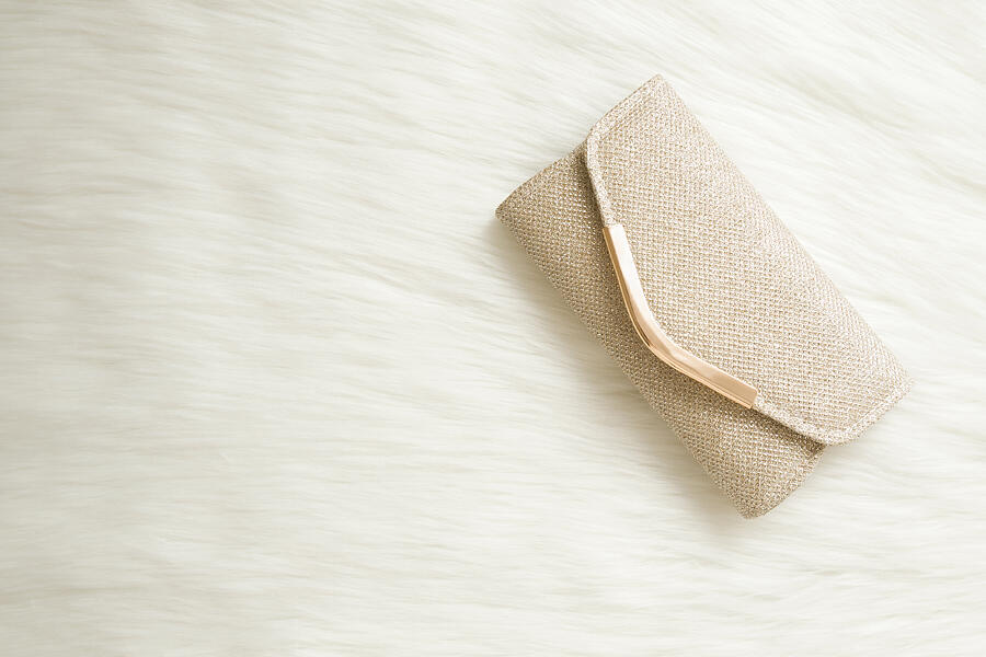 Shiny, golden clutch bag on white fluffy fur background. Woman accessory. Empty place for text. Closeup. Top down view. Photograph by FotoDuets