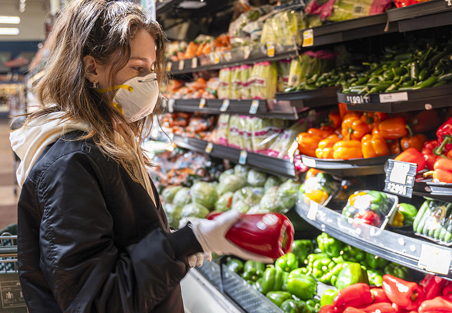 Shopping during a pandemic. A young woman wearing protective mask and gloves shopping vegetable in a store. Photograph by Alex Potemkin