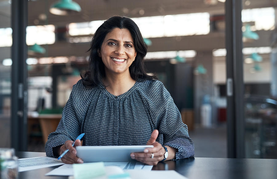 Shot of a mature businesswoman using a digital tablet and going through paperwork in a modern office Photograph by Shapecharge