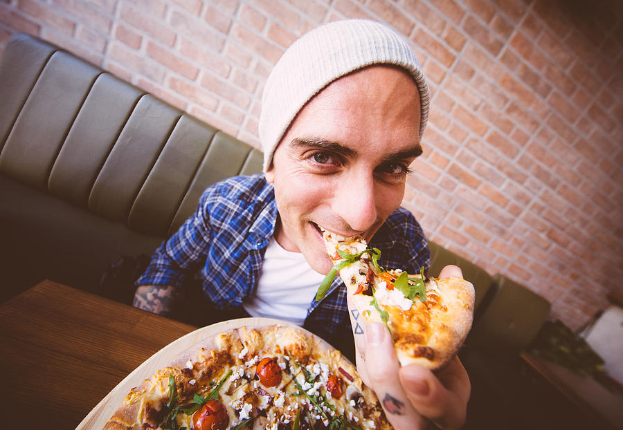 Shot of young man biting a slice of pizza Photograph by Wundervisuals