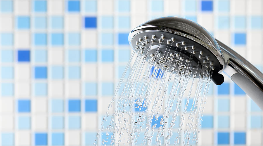 Shower head with flowing water stream in blue bathroom Photograph by Igoriss