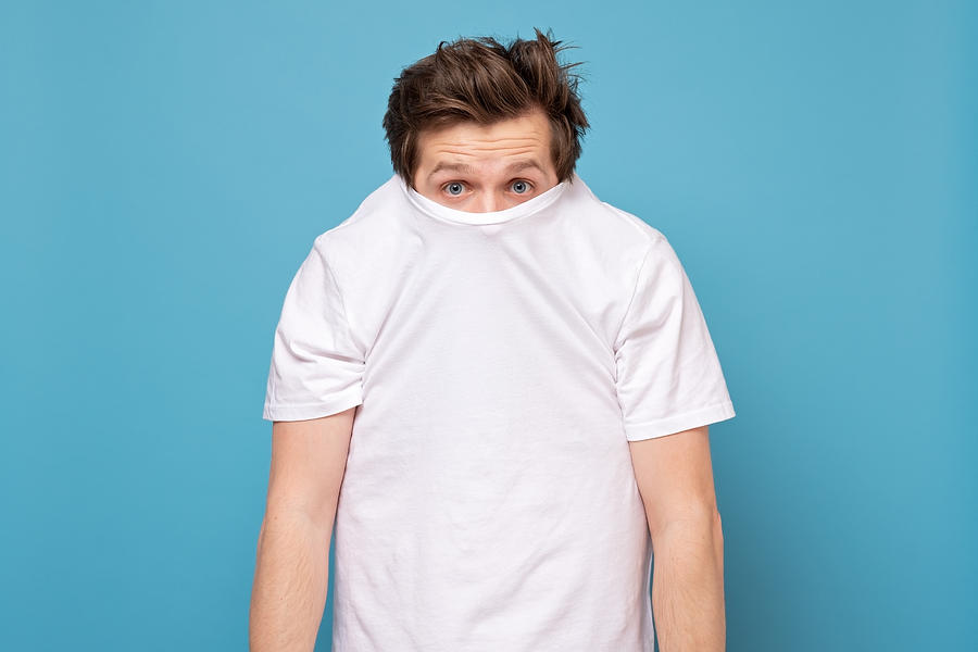 Shy caucasian man hiding behind his white shirt being afraid of coronavirus. Photograph by Koldunova_Anna