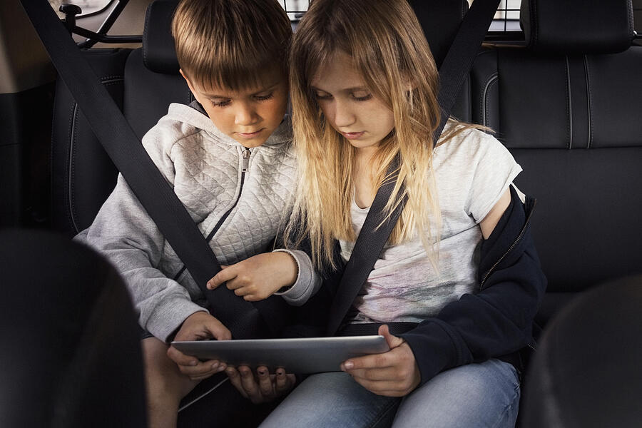 Sibling using digital tablet while sitting in electric car Photograph by Maskot