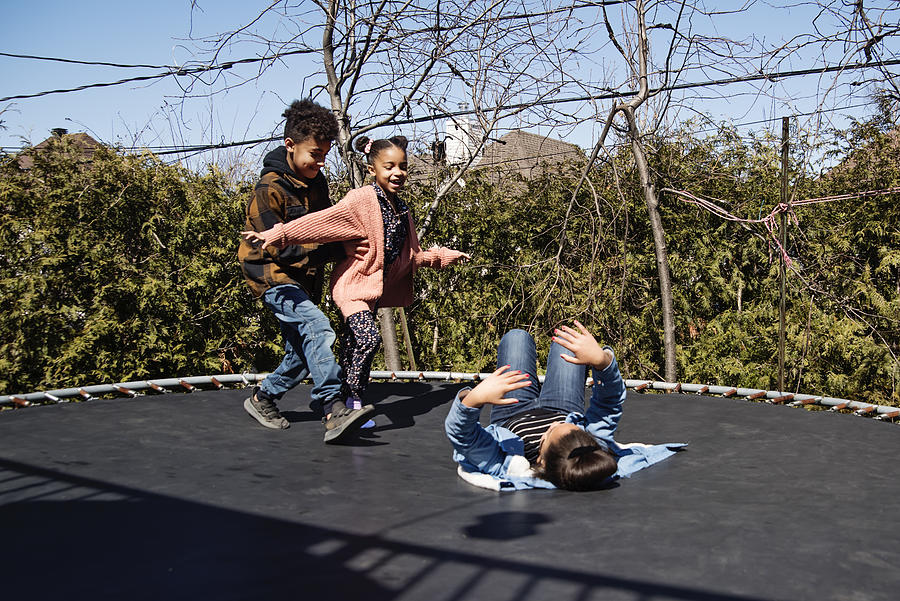 Siblings jumping on trampoline outdoors in springtime. Photograph by Martinedoucet