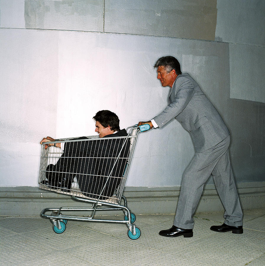 Side Profile Of A Businessman Pushing A Man In A Shopping Cart Photograph by George Doyle