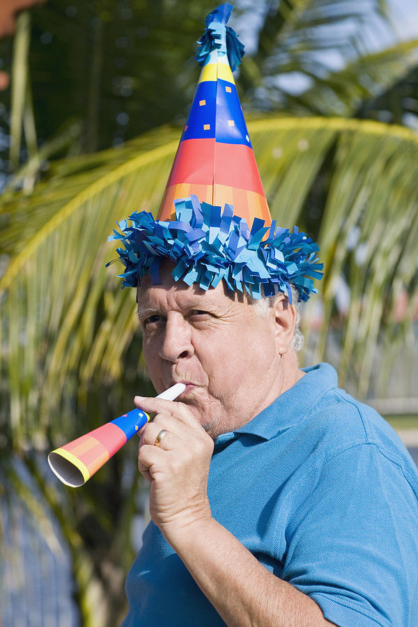 Side profile of a senior man blowing a party horn blower Photograph by Glowimages