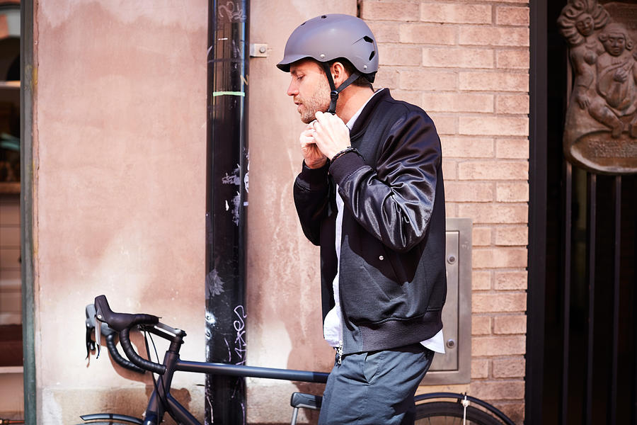 Side view of businessman wearing helmet while sitting on bicycle by wall at city Photograph by Maskot