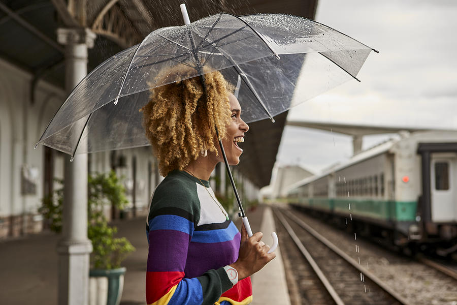 Side view of cheerful young woman enjoying while standing with umbrella at railroad station during monsoon Photograph by Westend61