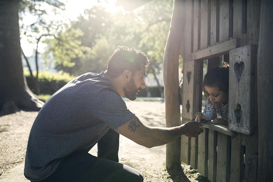 Side view of father and daughter playing in wooden toy house Photograph by Maskot